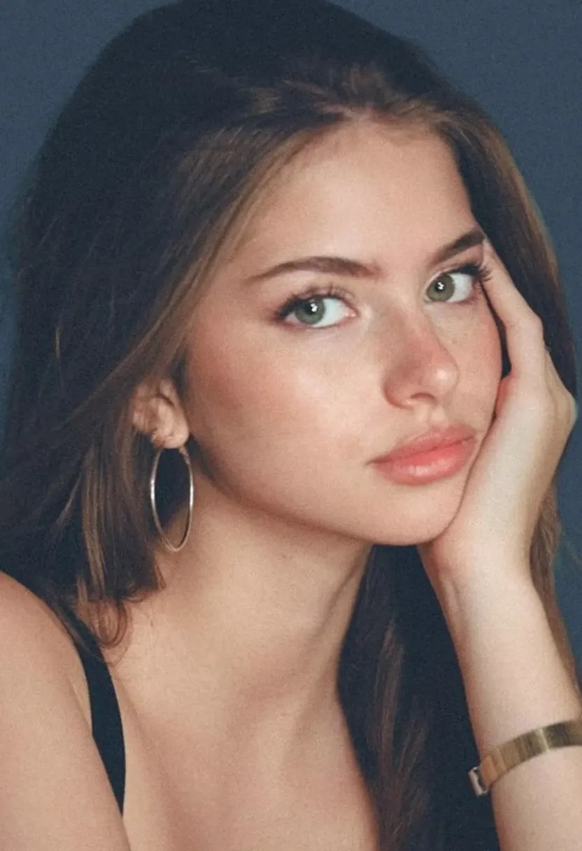Young woman with long brown hair, hoop earrings, and a black top against a dark background.