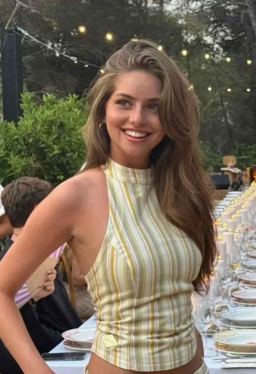 Young woman with long brown hair in a sleeveless high-neck striped top at an outdoor evening dinner setting.